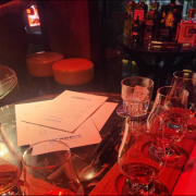 Glasses and documents are arranged on a bar table illuminated with warm red lighting.